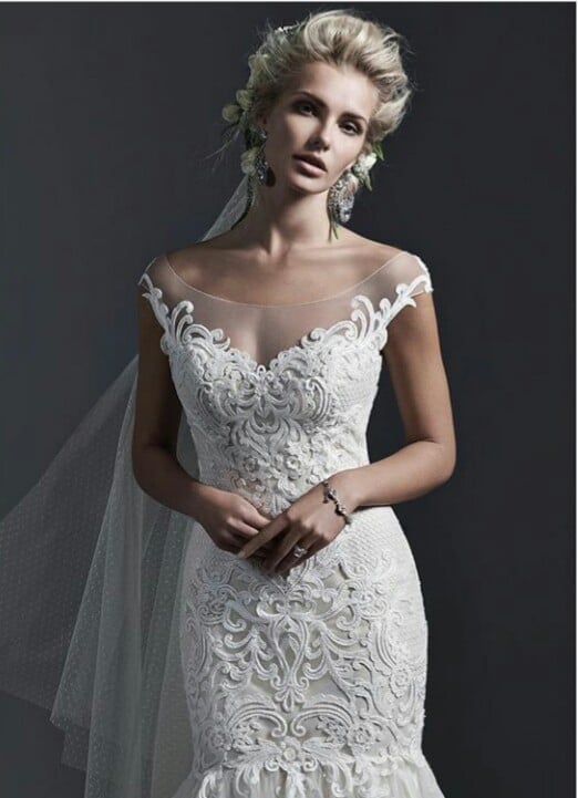Woman in ornate white lace wedding dress with off-shoulder neckline and flowing veil